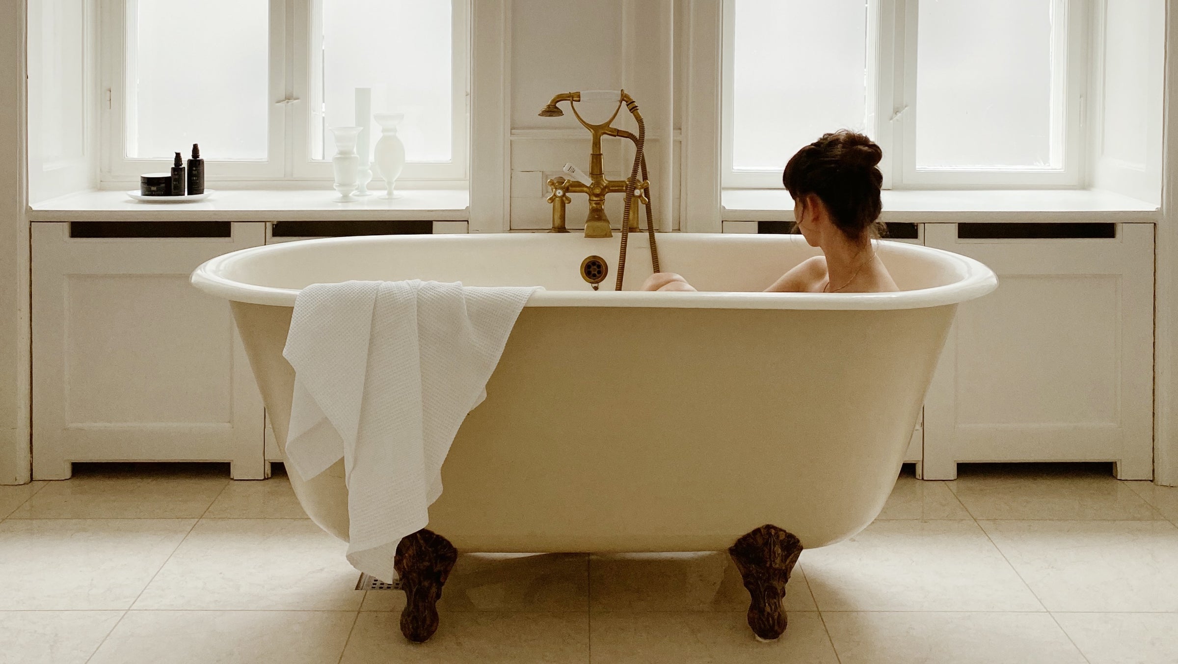 Kvinde, der tager et bad i vintage badekar med SMUK skincare økologiske hudplejeprodukter i vindueskarmen