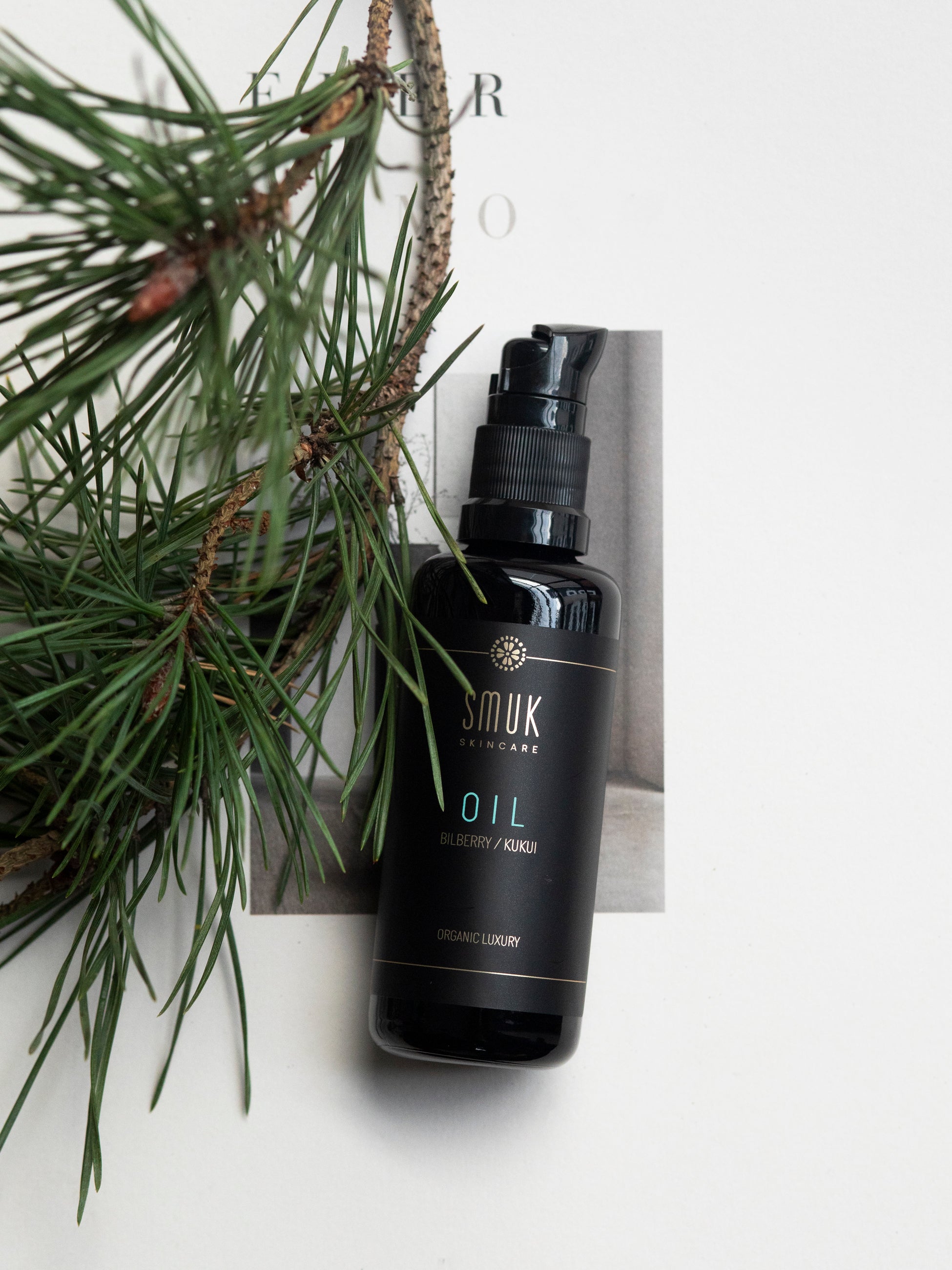 Sort flaske med SMUK skincare naturlig ansigtsolie på bord med fyrregren