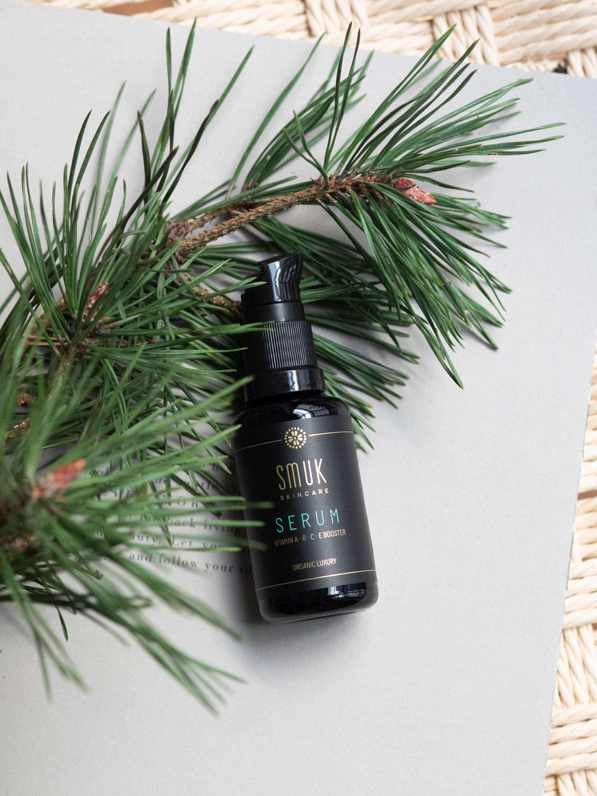 Sort flaske med SMUK skincare prisvindende vitaminserum på bord med fyrregren