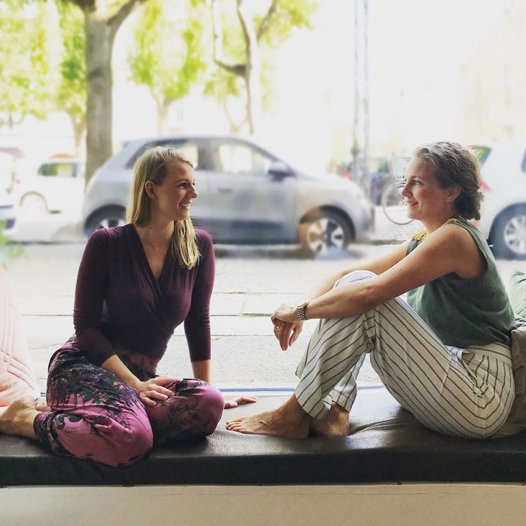 Kvinder i yogatøj taler og sidder på en bænk