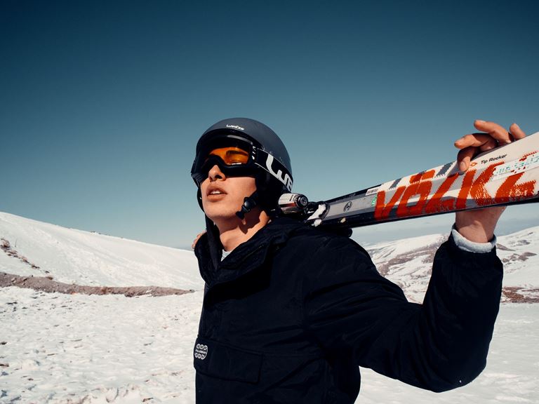 Kvinde i skihjelm holder sine ski bag nakken