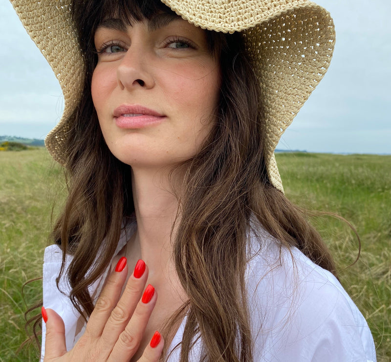 Kvinde udendørs i sommerlys med stråhat og naturlig hud med let glød