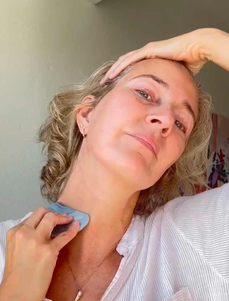 Kvinde bruger gua sha beauty tool på hals og ansigt som del af hudplejerutine