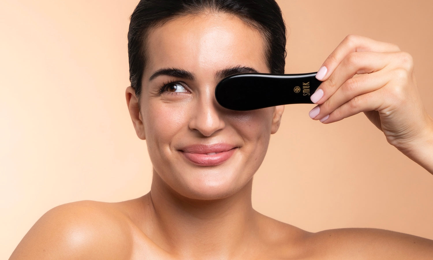 Smilende kvinde holder en gua sha-sten beauty tool foran øjet